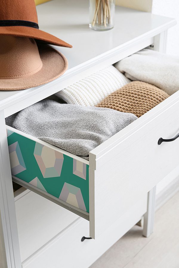 Chest of drawers with warm clothes and hats in room, closeup